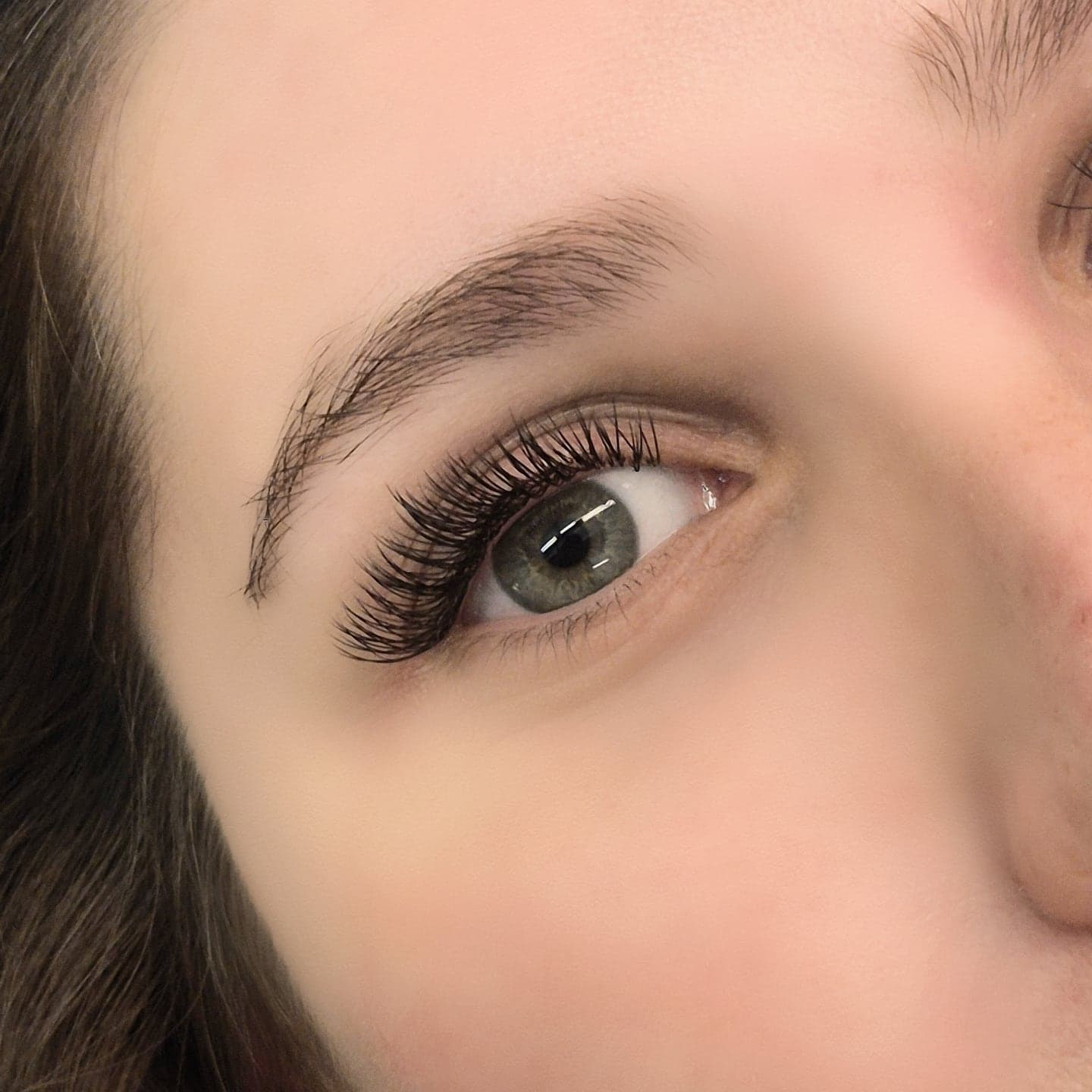 Glam lash extensions on a green eye with laminated brow